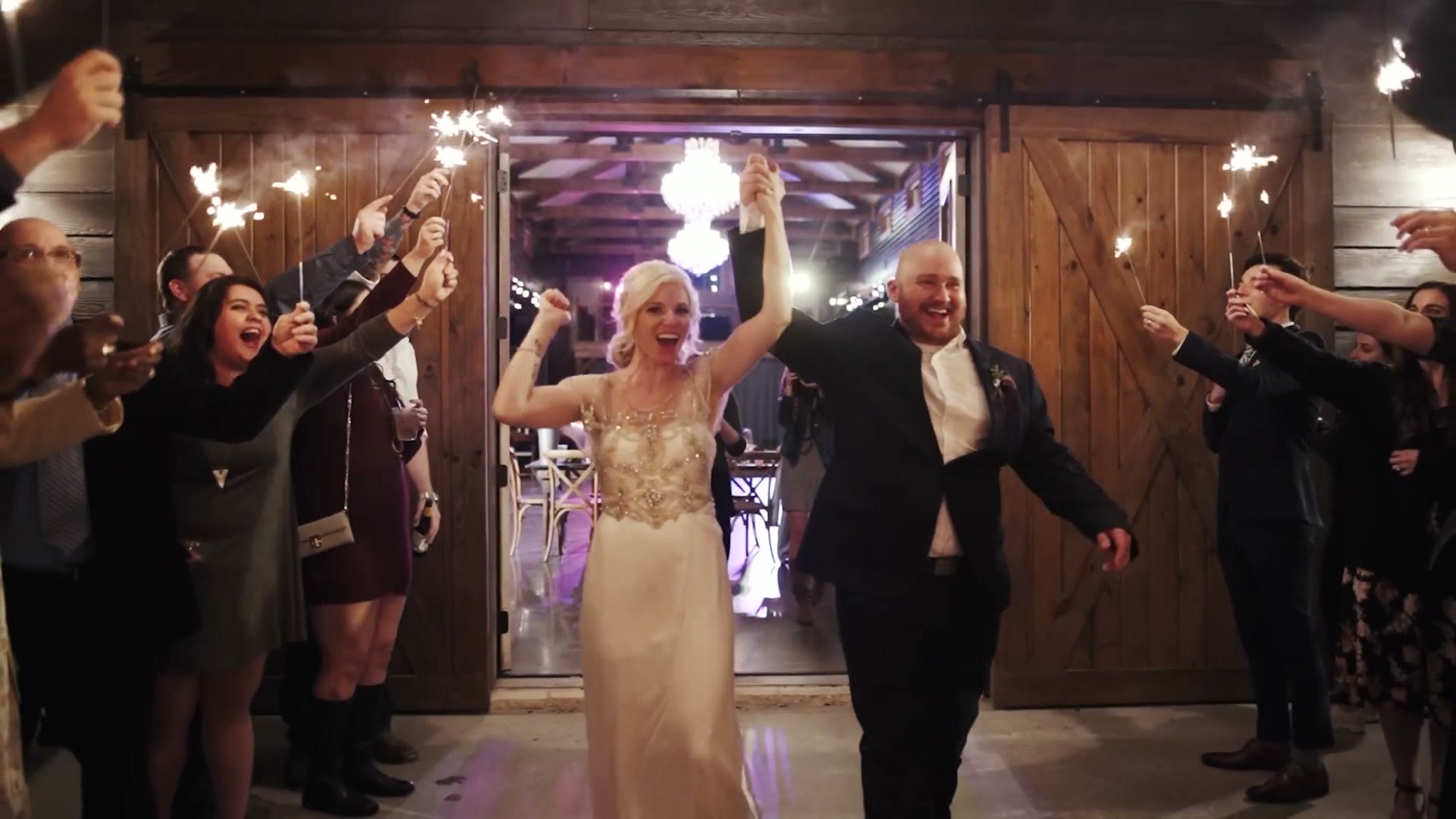 A bride and groom leaving a barn venue through a tunnel of guests holding sparklers