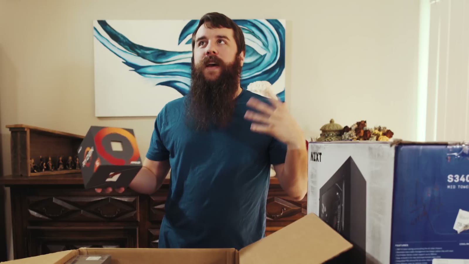 Matt holding an AMD Ryzen CPU box with a questioning expression, an NZXT case box behind him