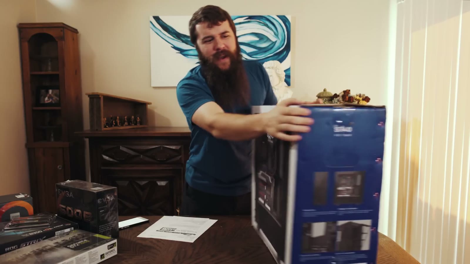 Matt lifting a large component box onto the table, the same blue abstract painting behind him