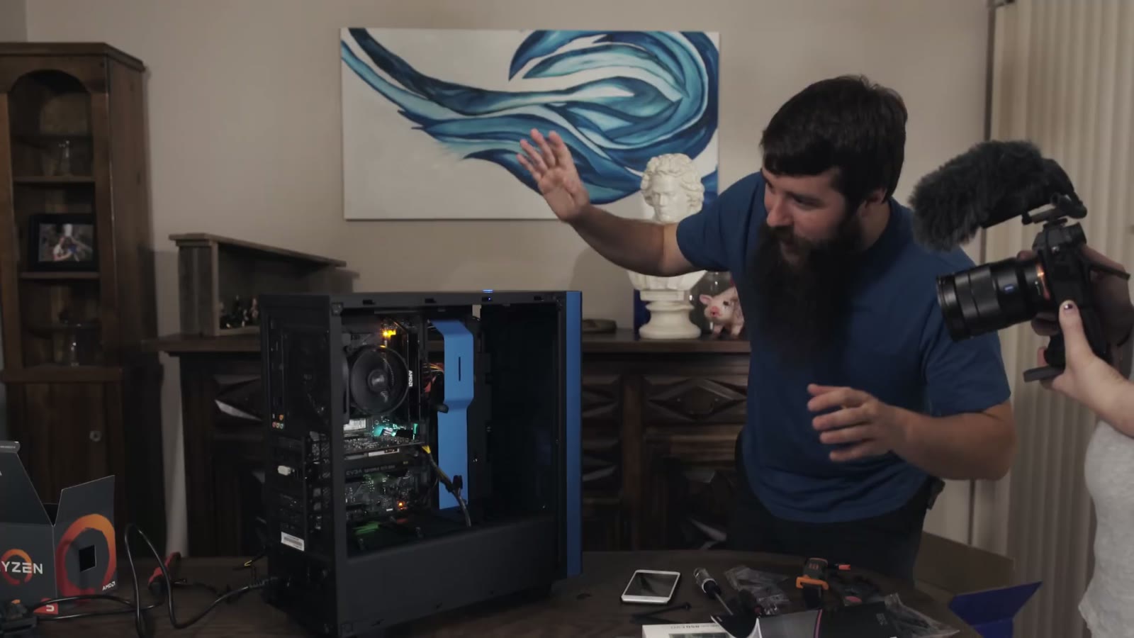 Matt gesturing beside the finished open PC case on the table while a camera operator films