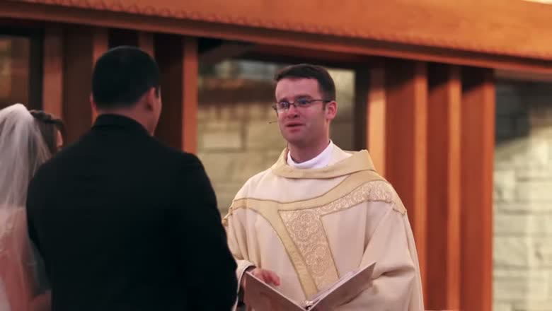 The priest reading from the missal during the Catholic ceremony, with the bride and groom standing in front of him