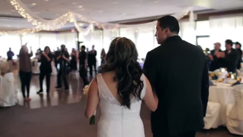 The bride and groom walking into their reception arm in arm as guests stand and applaud under string lights