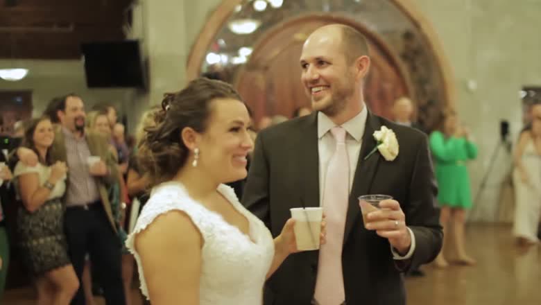 The bride and groom standing together at the reception with drinks in hand, laughing, surrounded by guests