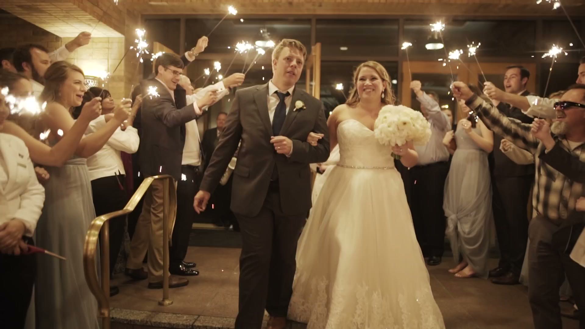A bride and groom walking out of their reception through a tunnel of guests holding sparklers at night
