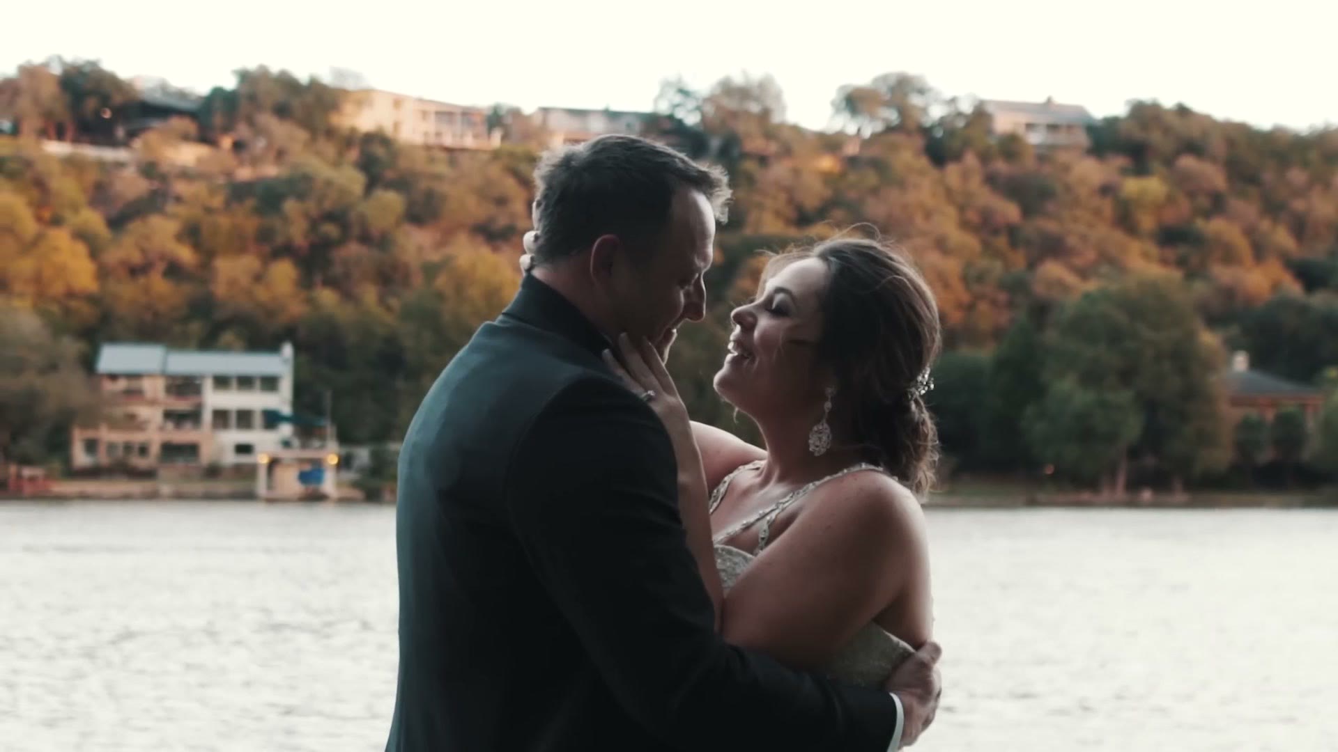 Bride and groom close together by the waters edge with autumn hills behind them