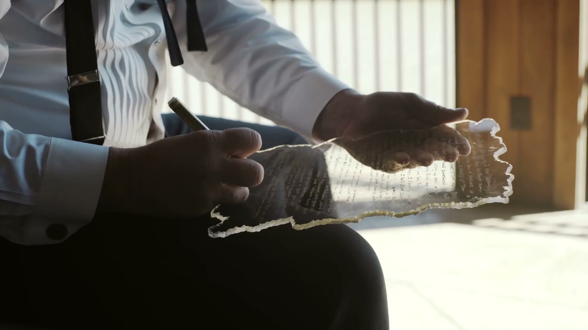 Groom sitting in bright window light, writing his vows on a torn edged sheet of paper