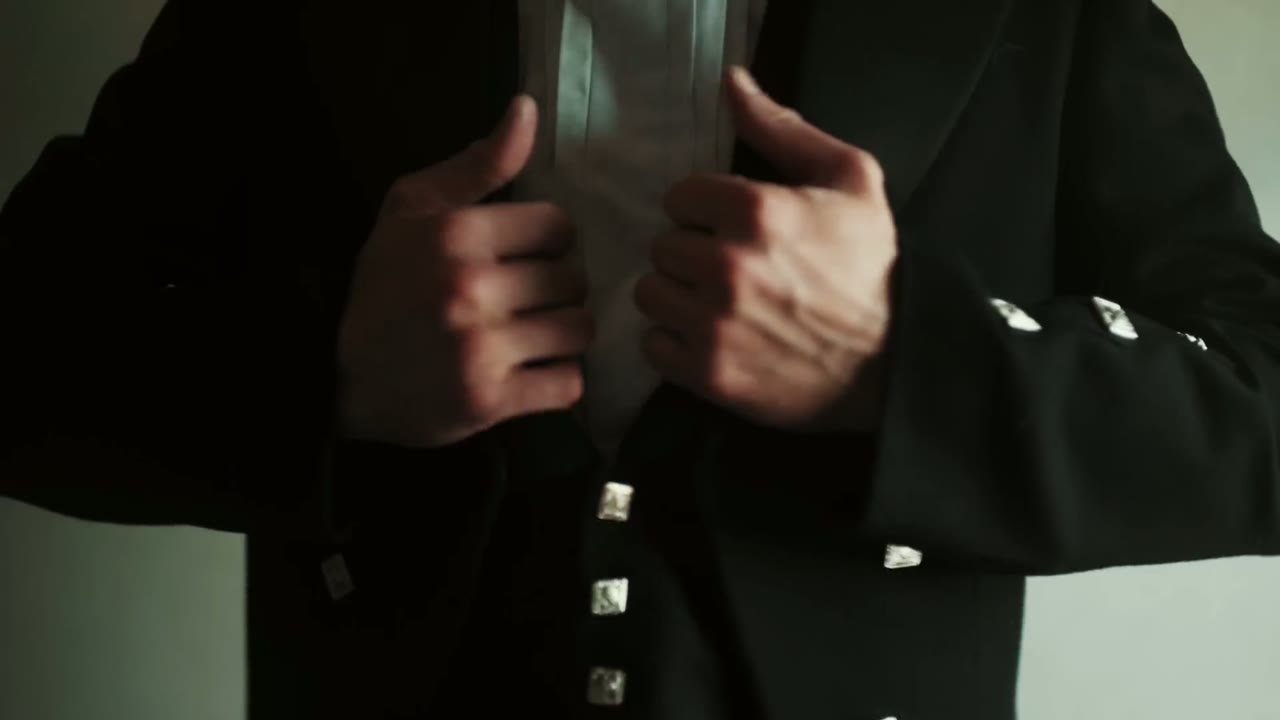 Close-up of hands buttoning a Scottish kilt jacket, silver buttons on the sleeve cuff and front