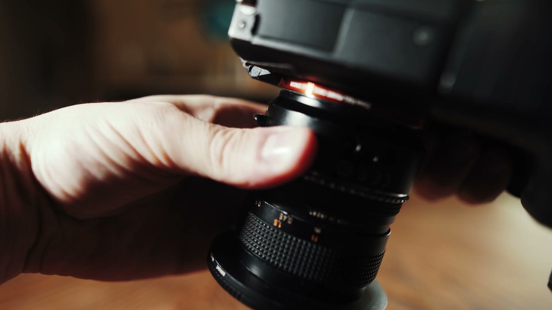 A hand twisting a lens off a camera that is being held with its mount pointing down toward the floor.