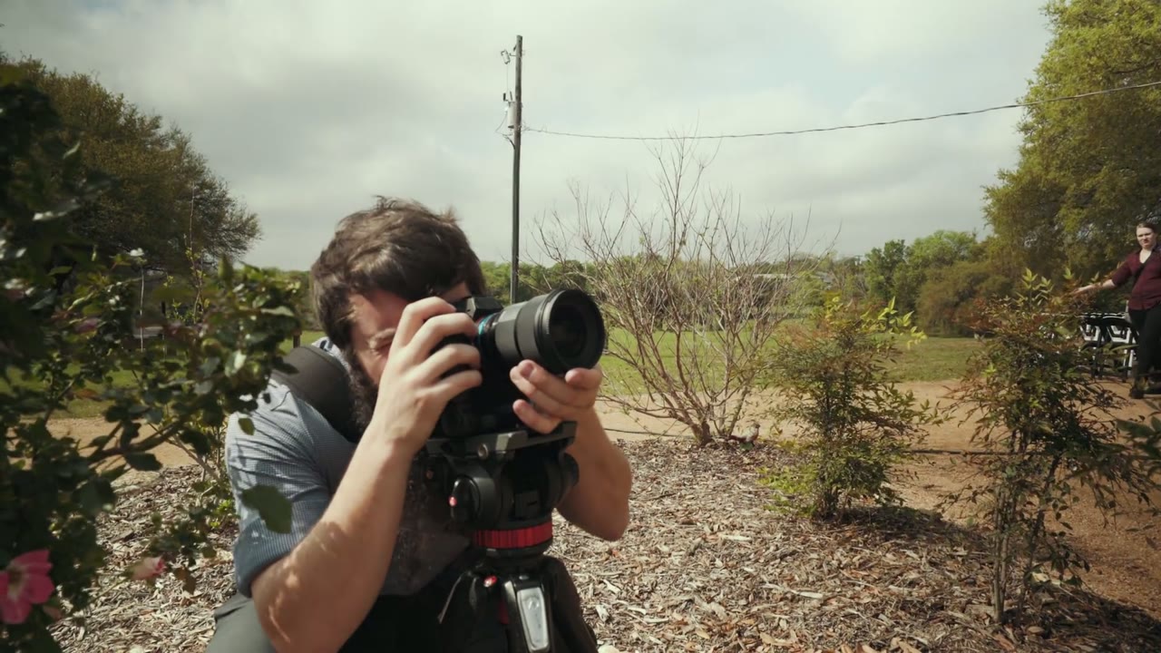 Matt looking through a telephoto camera on a tripod, framing a cloud time-lapse over an open field