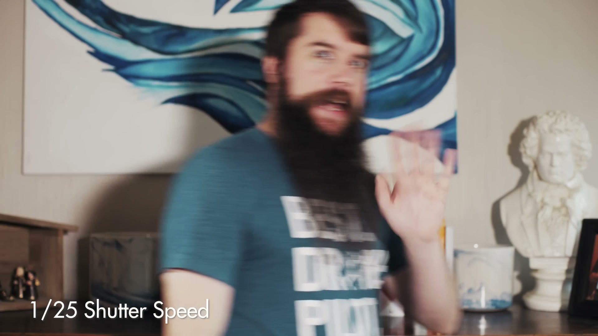 A badly smeared frame of Matt moving in front of a bookshelf, labelled 1/25 Shutter Speed