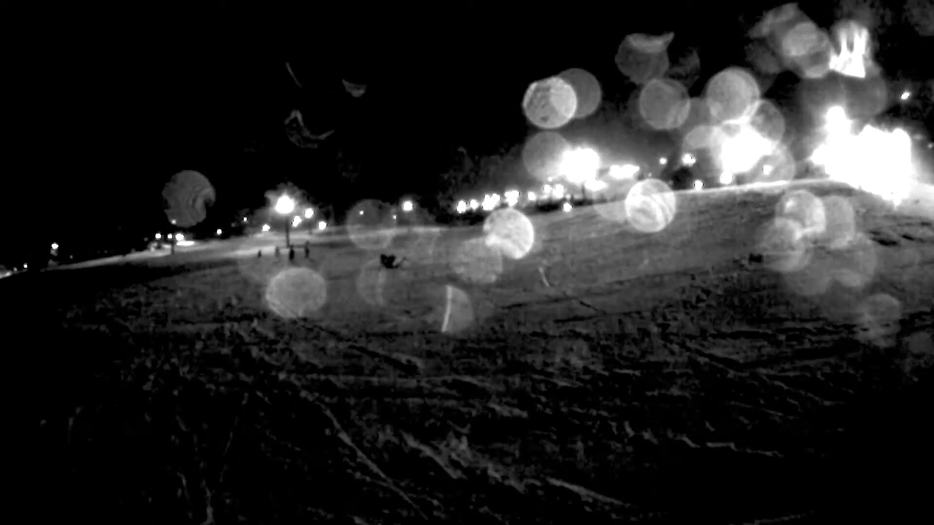 A ski run at night lit by floodlights along the edge, with rain on the camera lens turning each light into a soft circle of glare