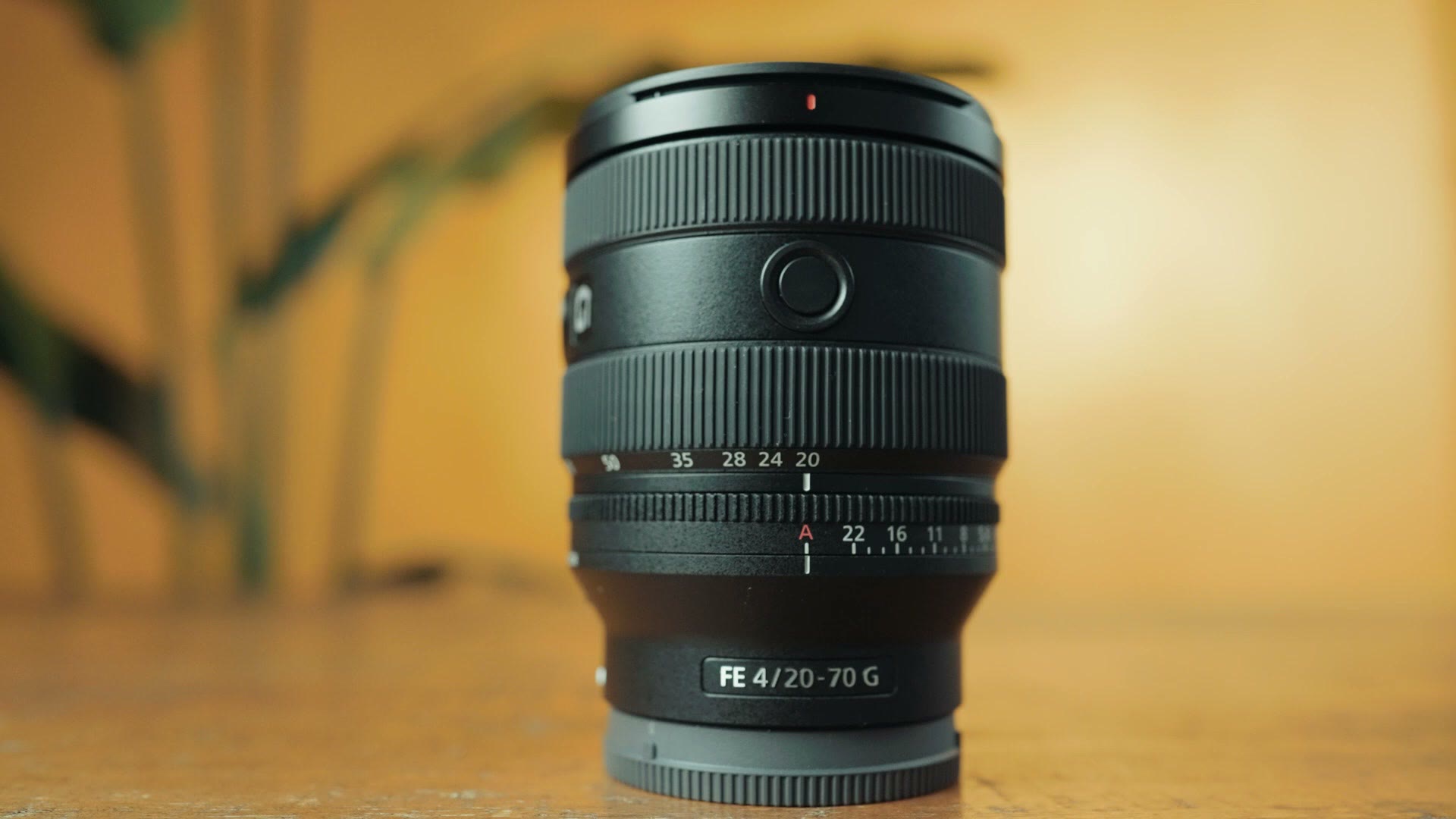 Sony FE 20-70mm F4 G lens standing on a table in front of a yellow backdrop