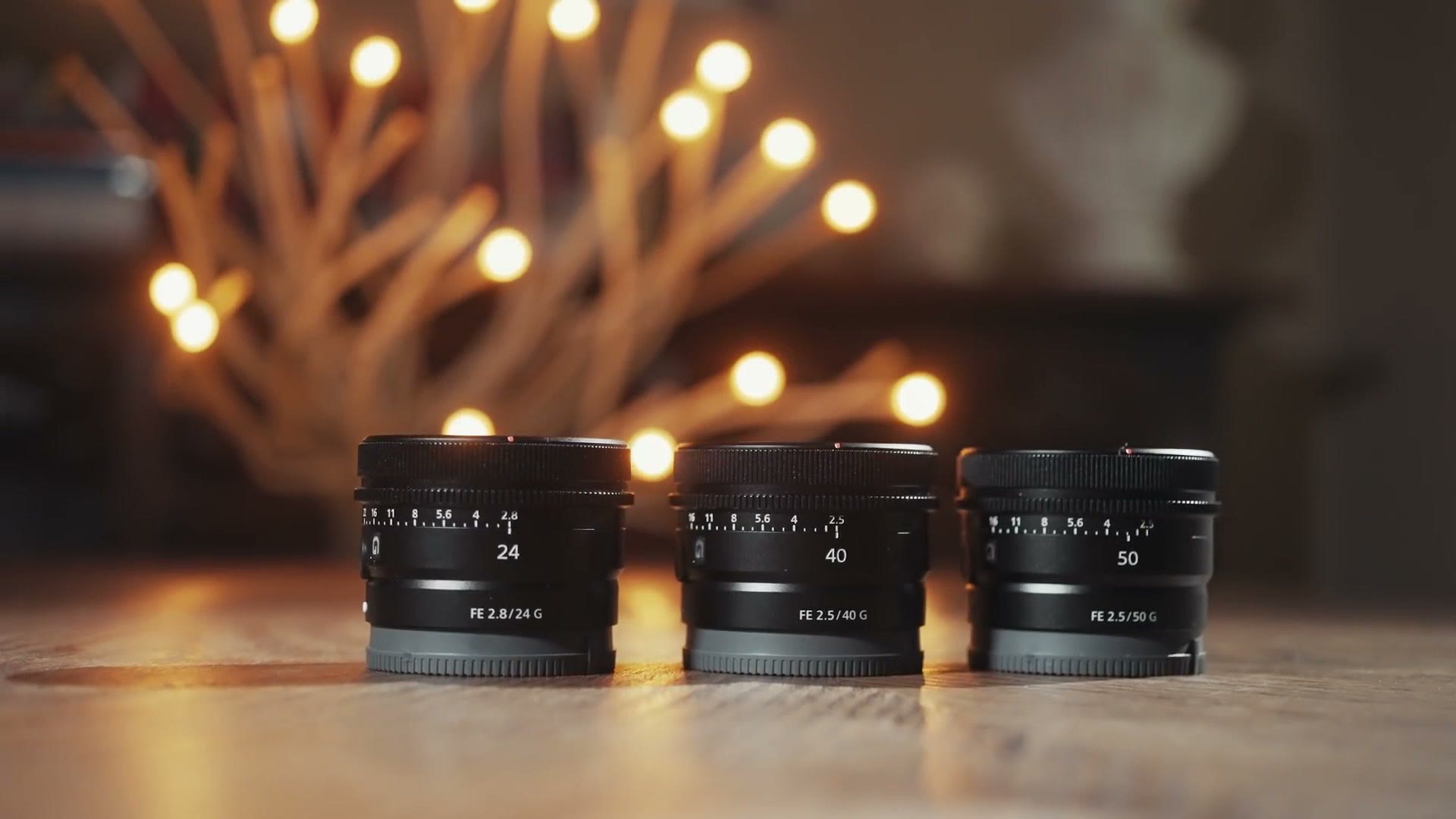 The Sony FE 24mm f/2.8 G, 40mm f/2.5 G and 50mm f/2.5 G standing in a row on a wooden table