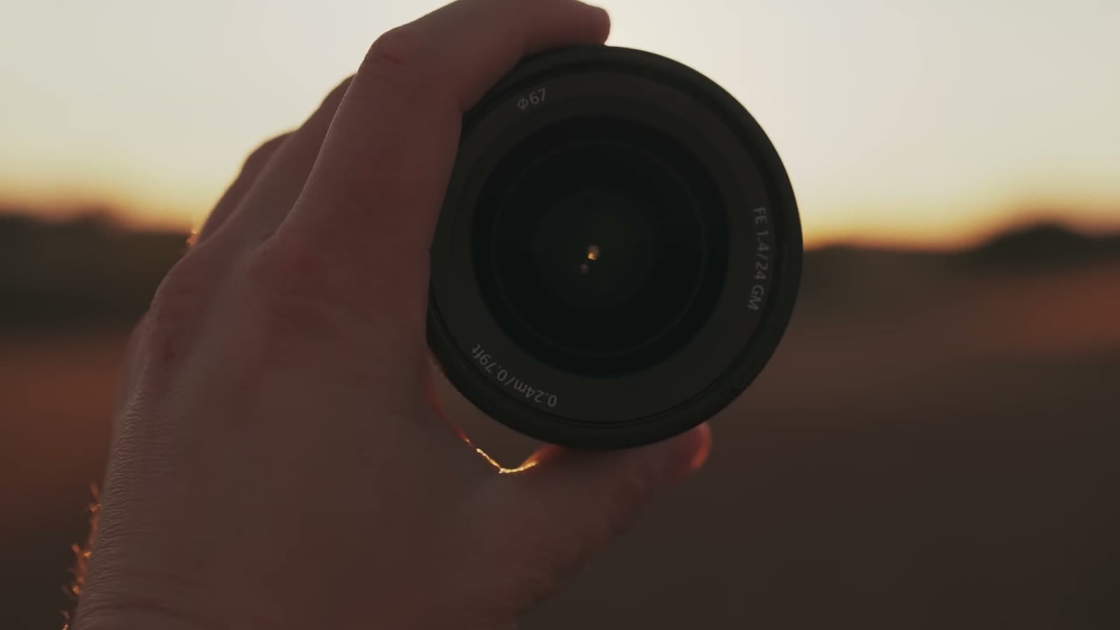 The Sony 24mm GM held front on, showing a 67mm filter thread and a 0.24 metre minimum focus distance printed on the barrel