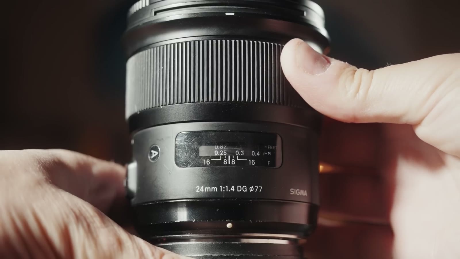 A hand resting on the barrel of a Sigma 24mm f1.4 DG lens, showing how much larger it is