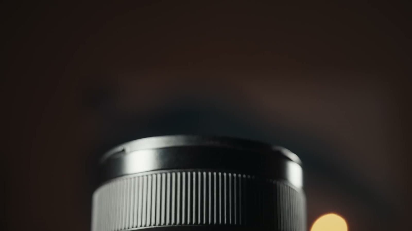 The Sony 24mm GM lens photographed in near darkness with only a rim of light on the barrel