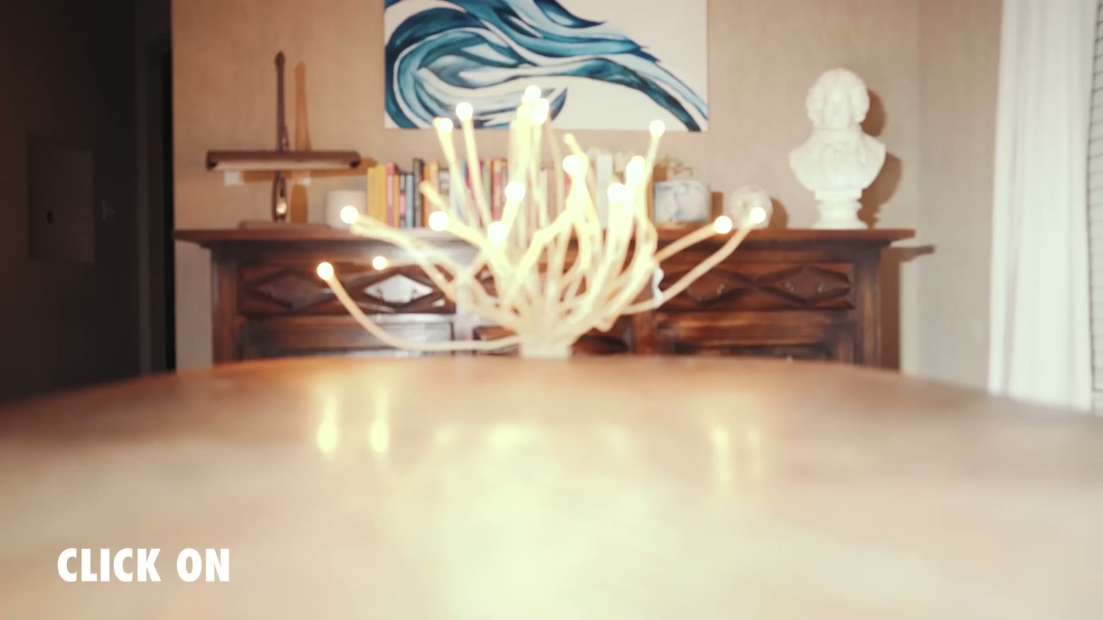 A lamp of fine glowing filaments on a table shot wide open, with the words CLICK ON on screen