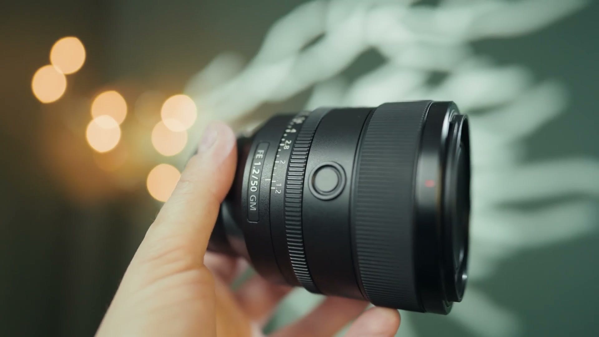 The Sony FE 50mm f/1.2 GM held in one hand with bokeh behind it