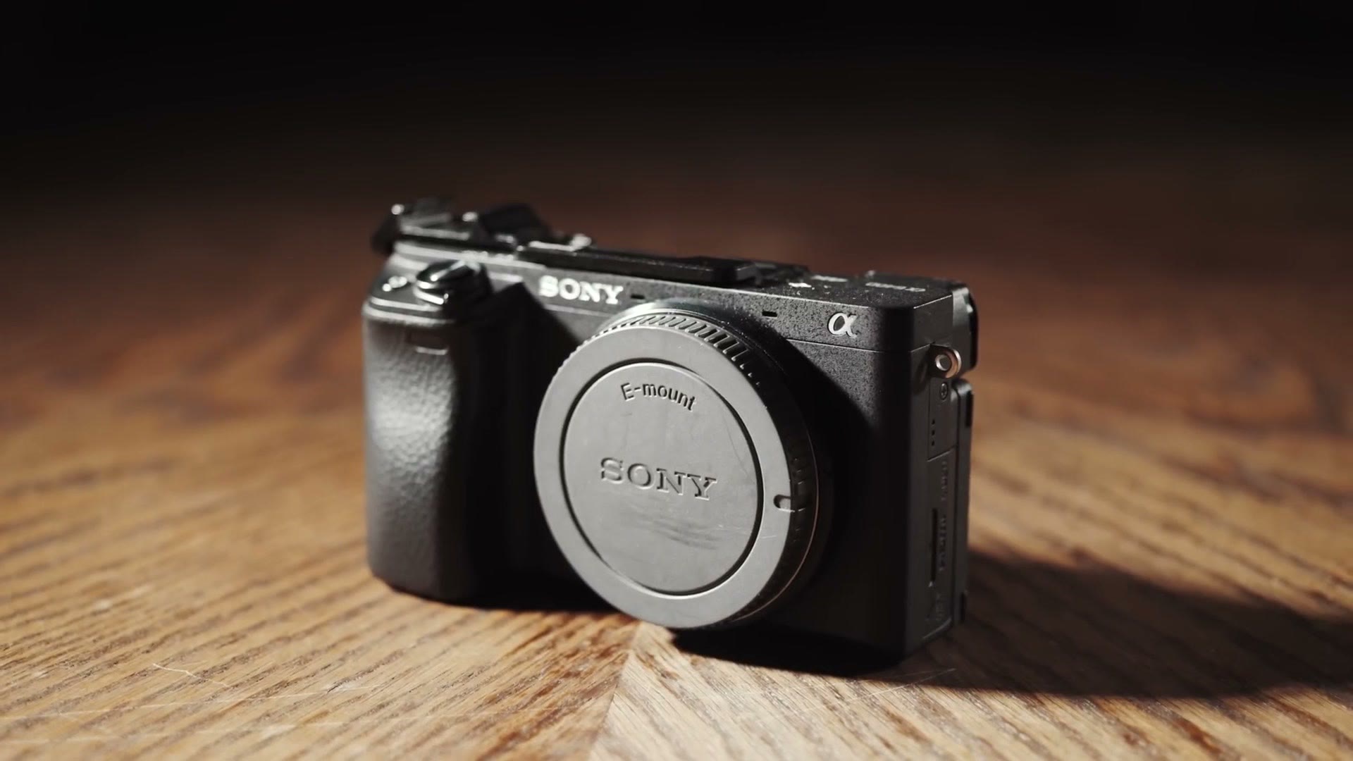 Close-up of a black Sony a6400 camera body with rear cap on, resting on a wooden table