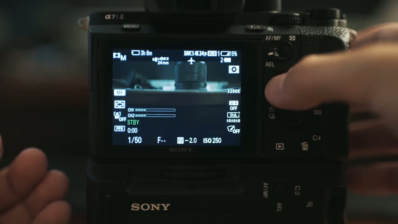 Sony a7S II standby screen showing XAVC S 4K24p, ISO 250, and 15% battery with a thumb near the AEL button