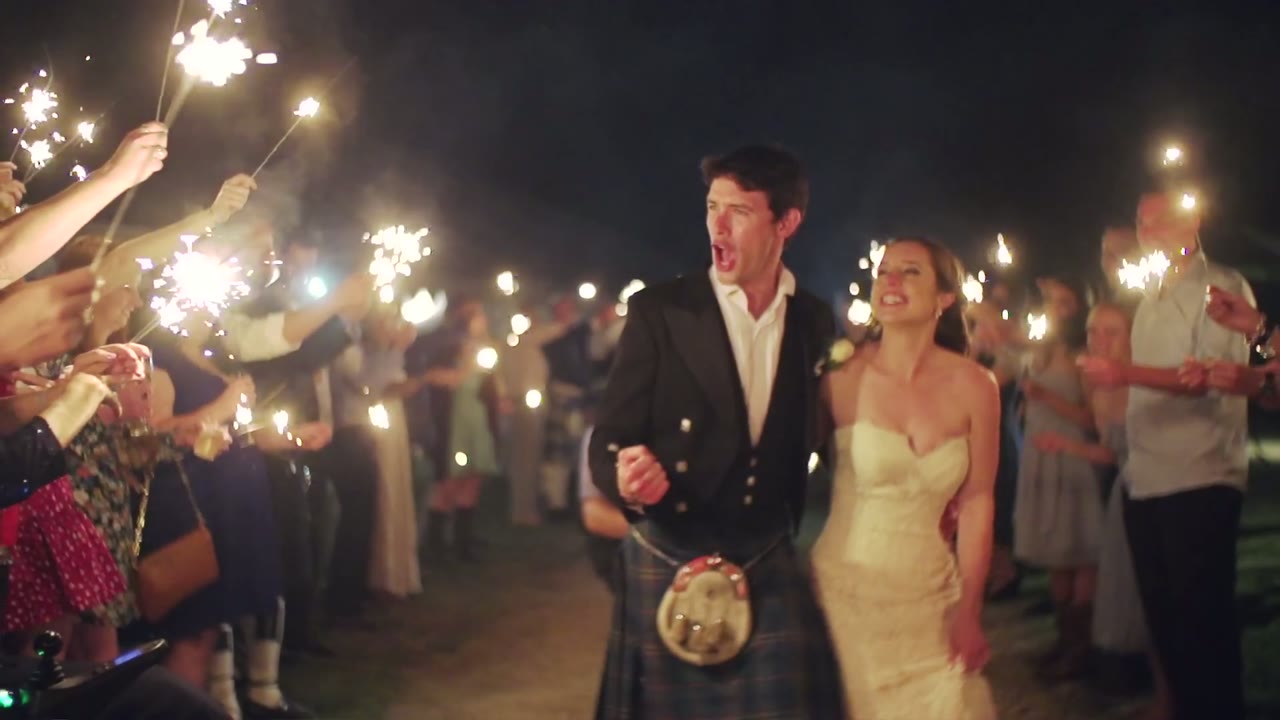 Bride and groom laughing as they exit through a sparkler tunnel at night, guests lining both sides
