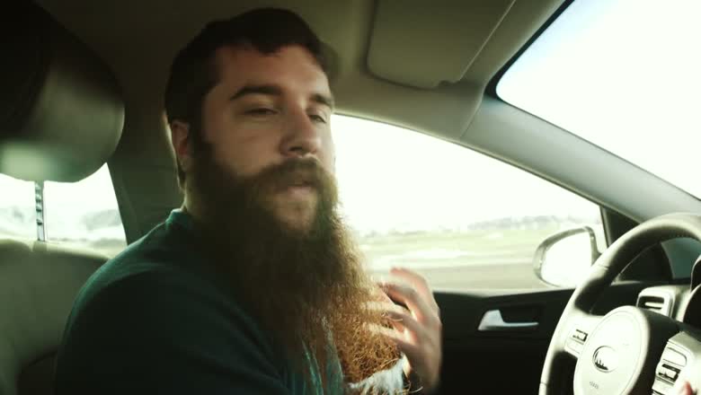 Talking to camera from the driver's seat of a rental car, with flat Icelandic countryside out the passenger window