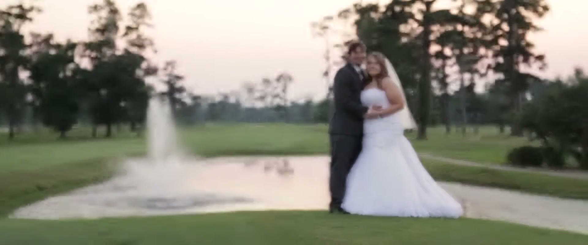 The bride and groom standing together beside a fountain on the golf course at dusk, with pines behind them