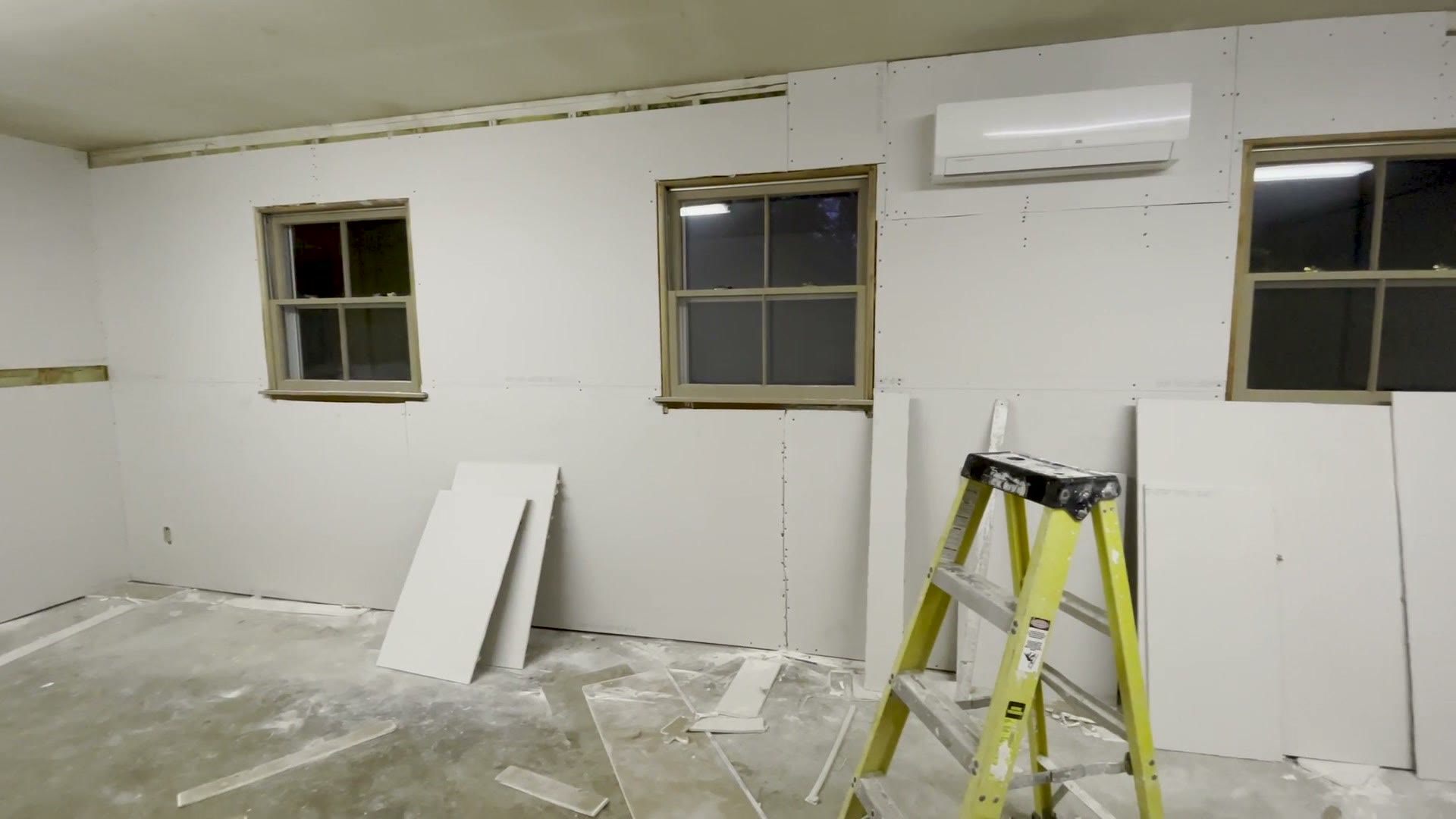 The finished blank room with new drywall, painted white, with a mini split AC unit on the wall