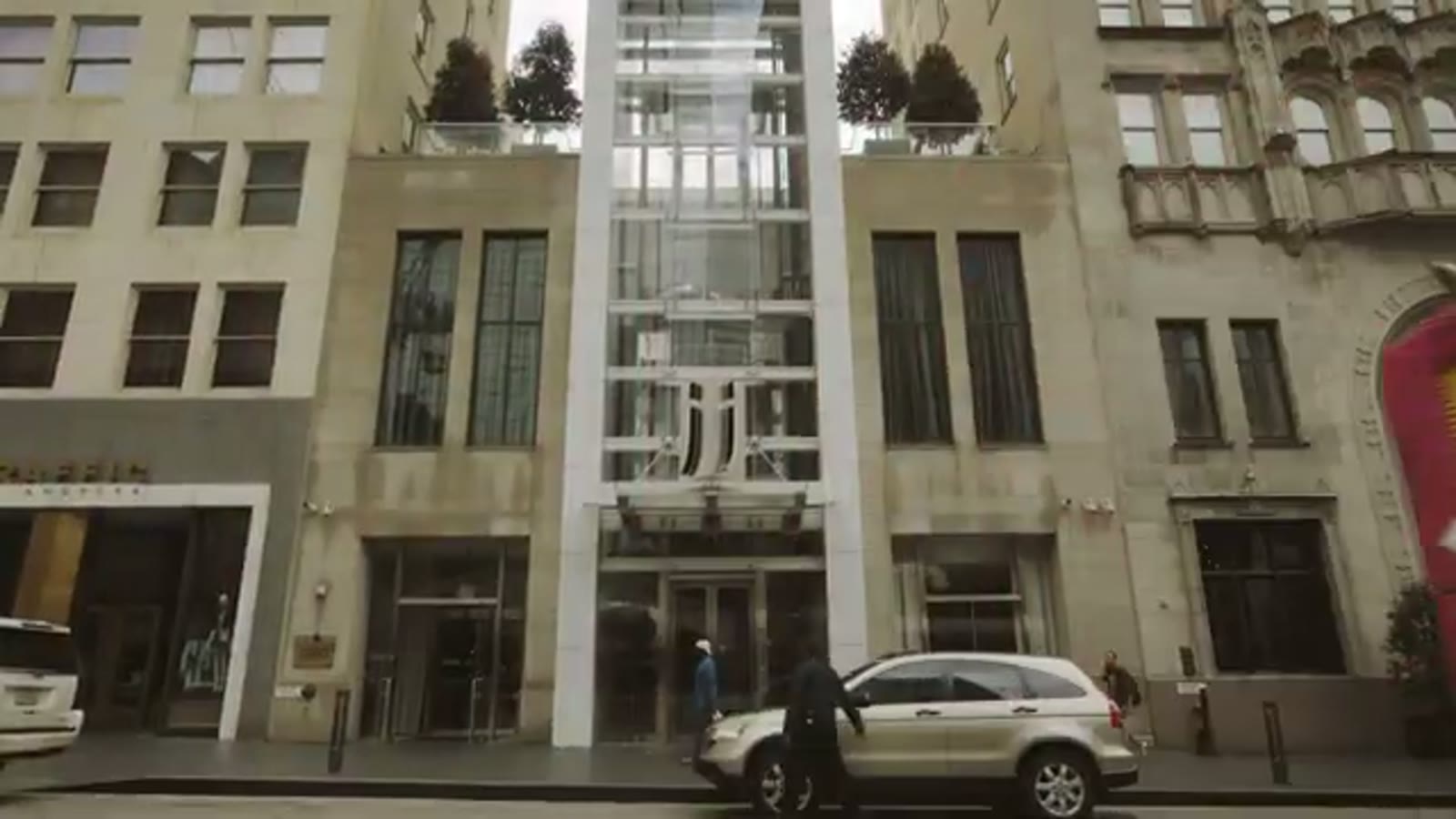 Street view of the glass-fronted Joule Hotel entrance in downtown Dallas with a car parked out front