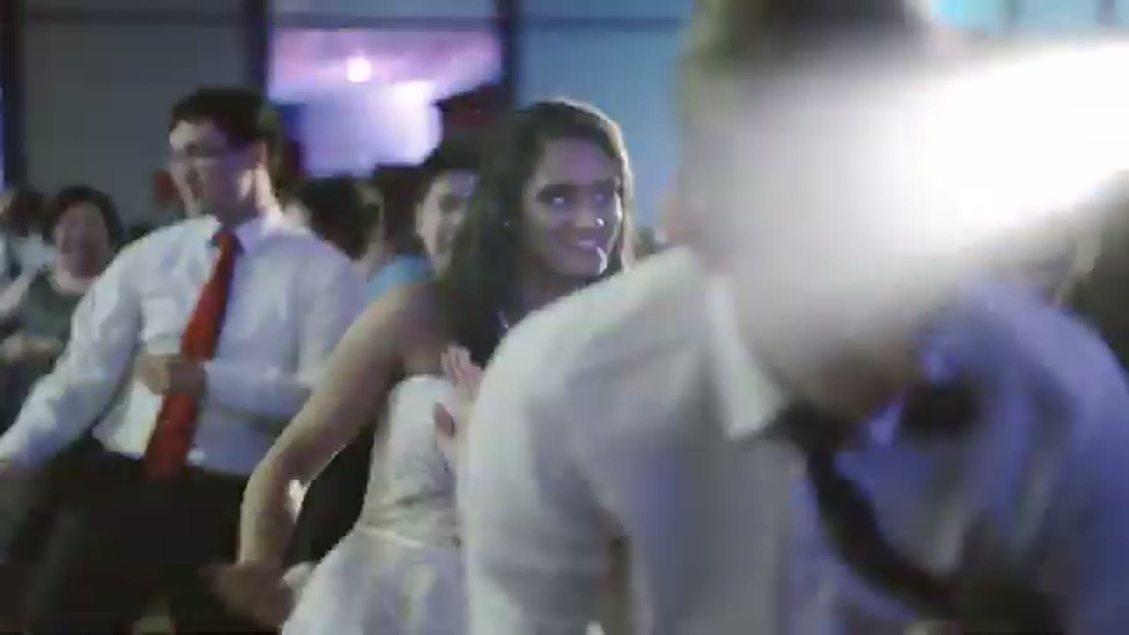 Bride smiling over her shoulder while dancing among guests at the reception, motion-blurred lights around her