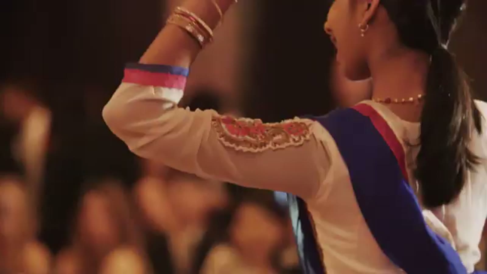 Close-up of a bridesmaid's arm raised mid-dance, showing gold bangles and an embroidered sari sleeve
