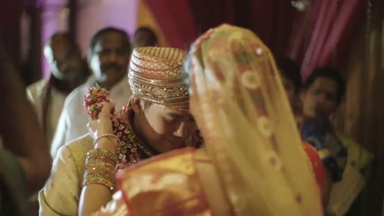 Groom in a beaded cap and bride in gold veil pressing foreheads together during the Indian ceremony