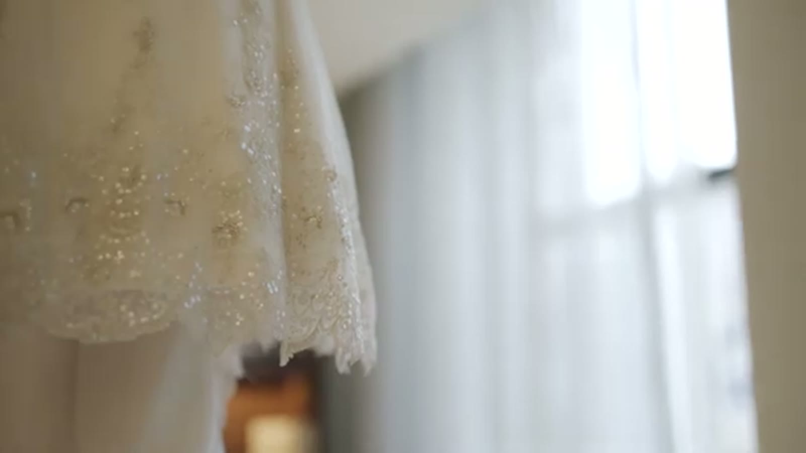 Close-up of a beaded lace wedding dress hem hanging in front of a bright window