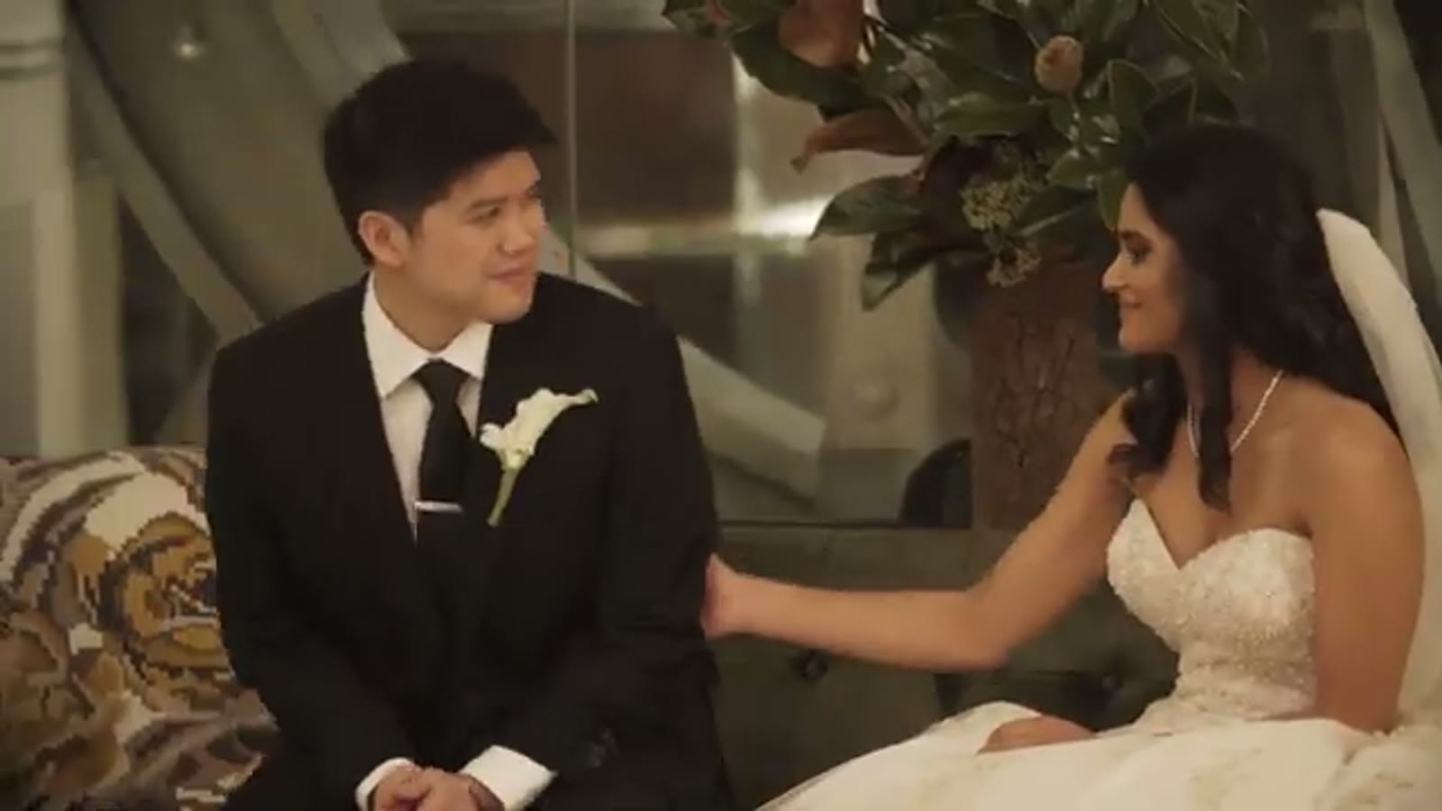 Bride reaching to touch the groom's hand as they sit together on a patterned sofa, both smiling