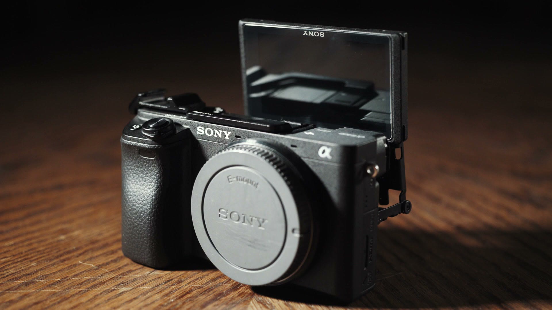 A Sony a6400 body on a wooden table with its rear screen flipped up over the top of the camera