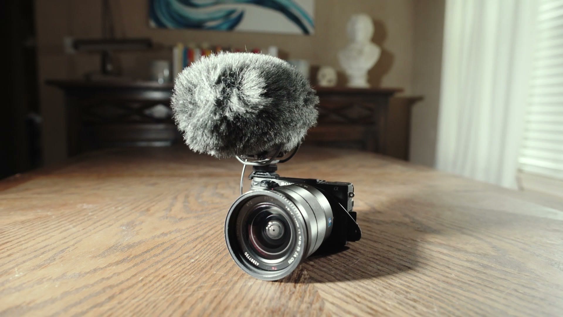 A small Sony mirrorless camera on a table with a Rode VideoMic Pro Plus and its furry windshield mounted on top