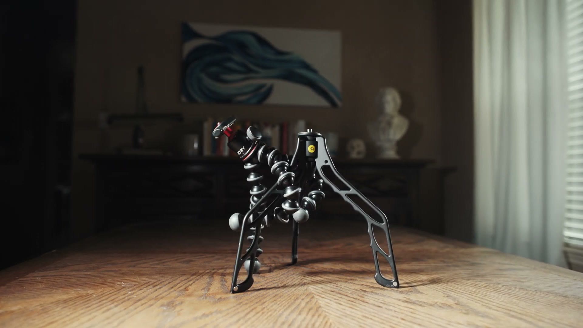 A Switchpod with its three feet flipped out standing beside a Gorillapod on a wooden table, both with ball heads fitted