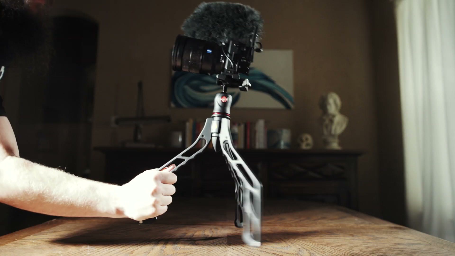 A hand lifting a Switchpod off a table with a camera and a shotgun microphone mounted on it