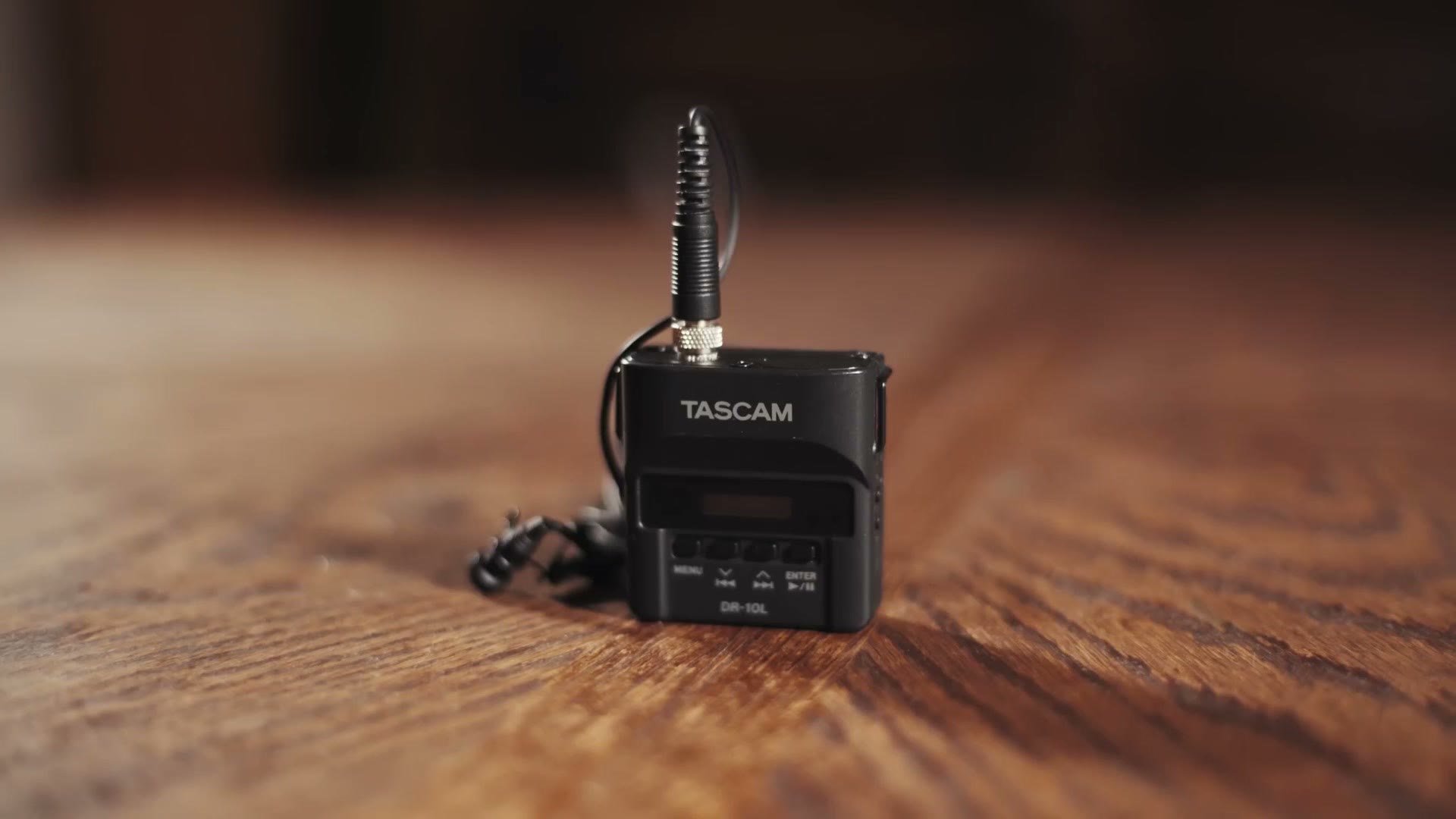 Tascam DR-10L recorder with lavalier mic cable, sitting on a wooden table