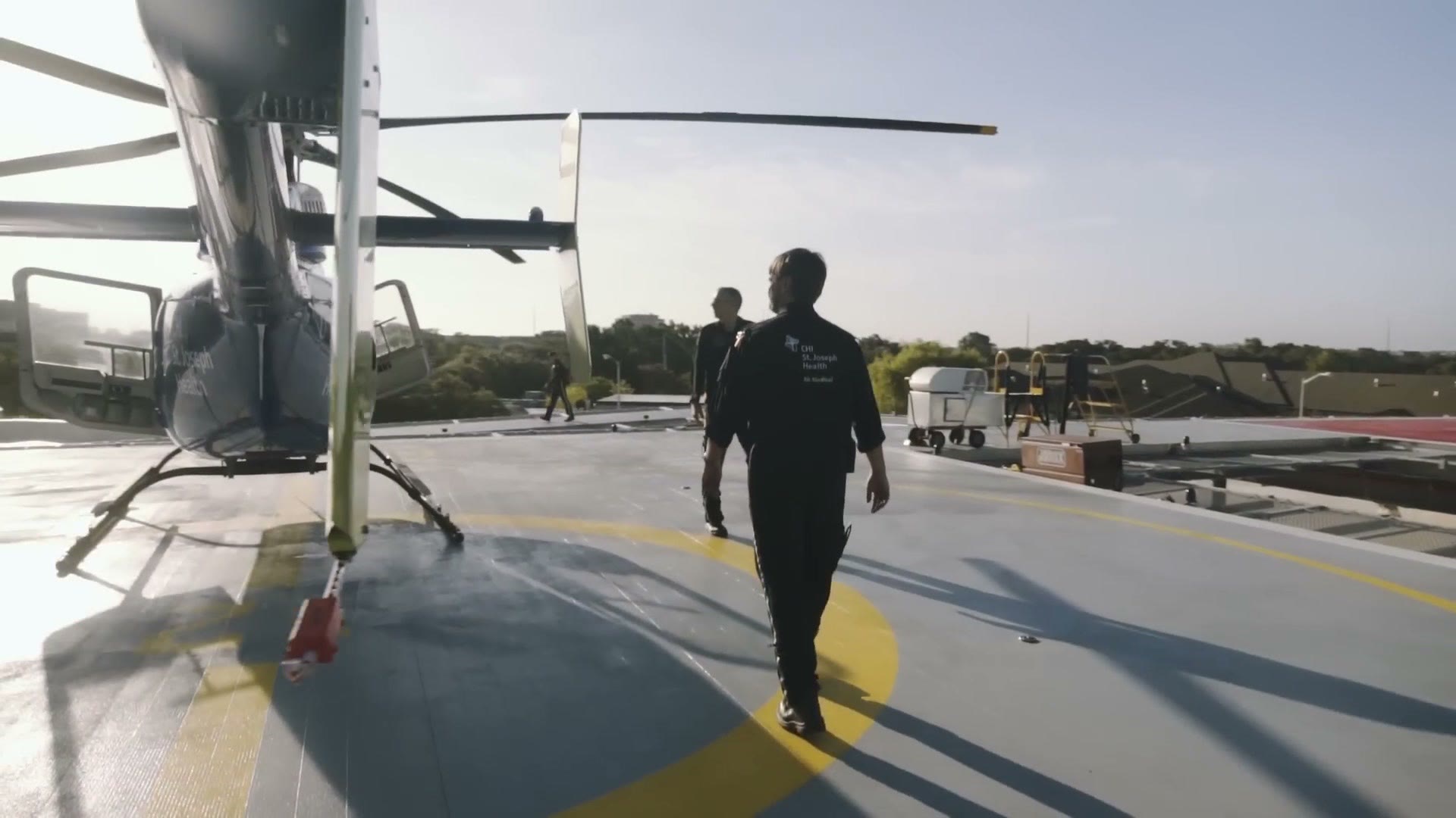 Flight crew walking across a rooftop helipad toward a medical helicopter with its rotors turning