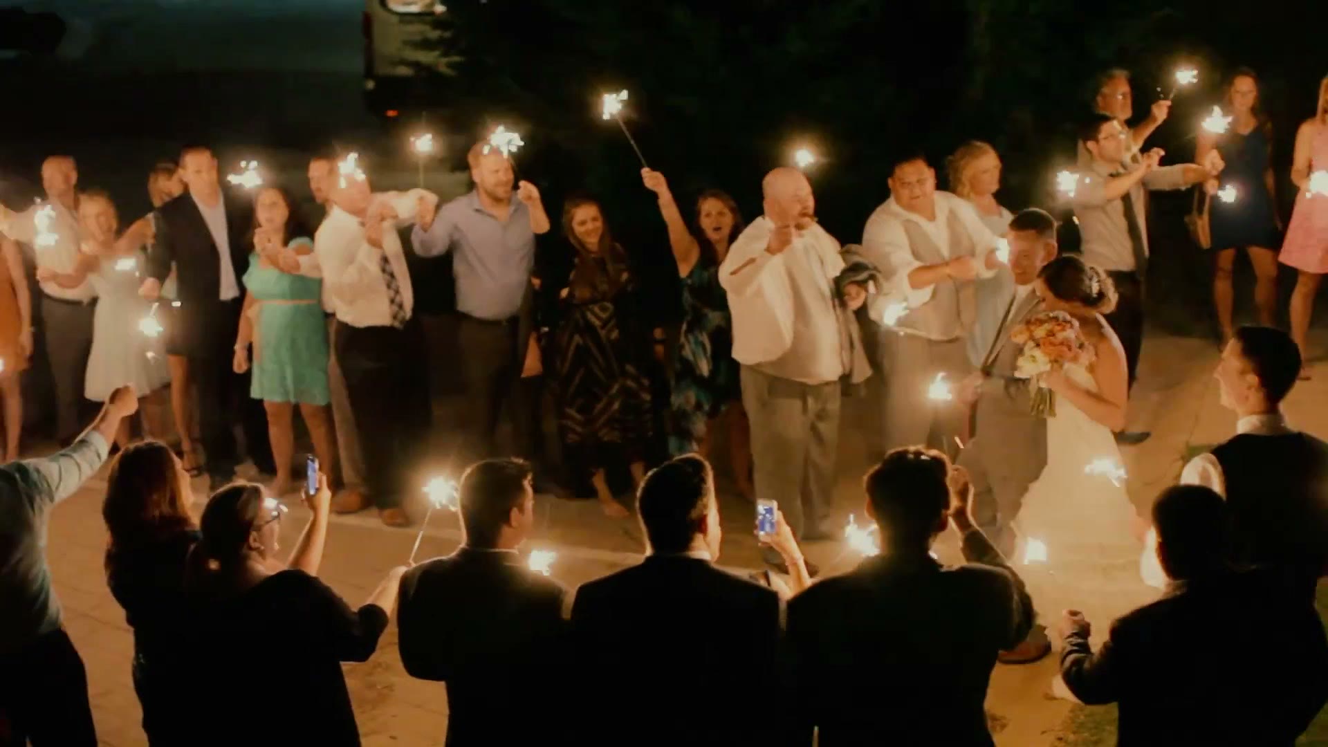 Wedding guests lining a path at night holding lit sparklers as the couple walk out between them