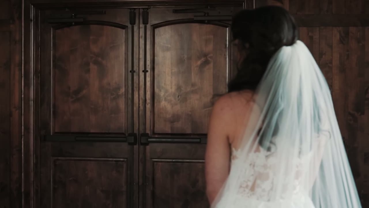 Bride in her veil seen from behind, walking toward large wooden double doors