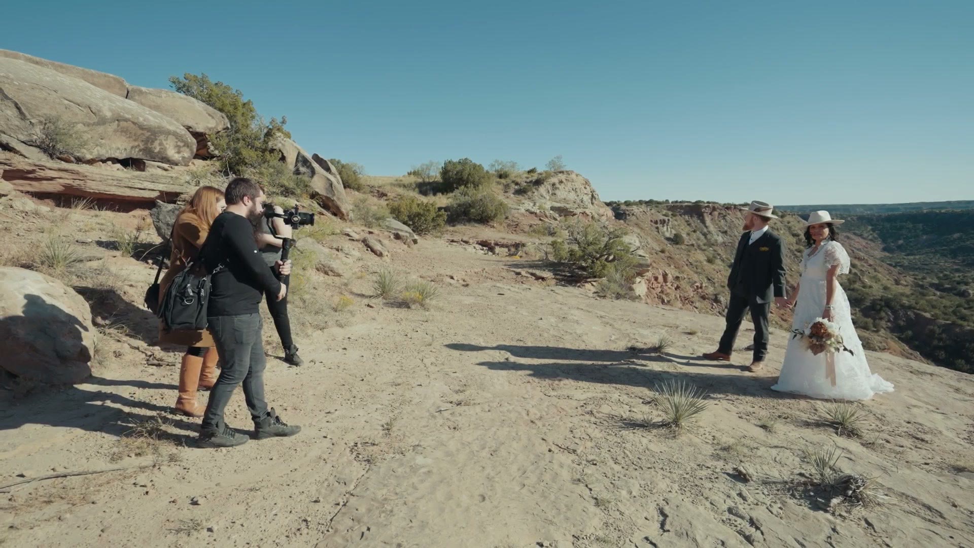 Behind the scenes of a wedding couple being filmed on a cliff at sunset