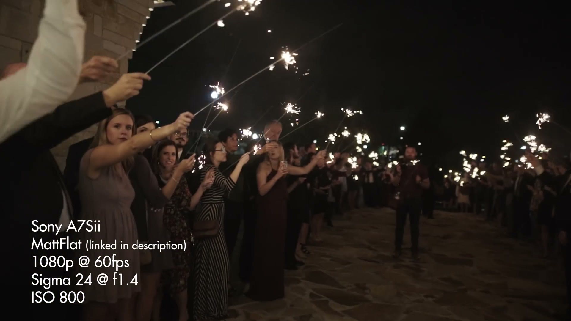 Guests lighting sparklers along both sides of a walkway at night, seen from in front of the couple