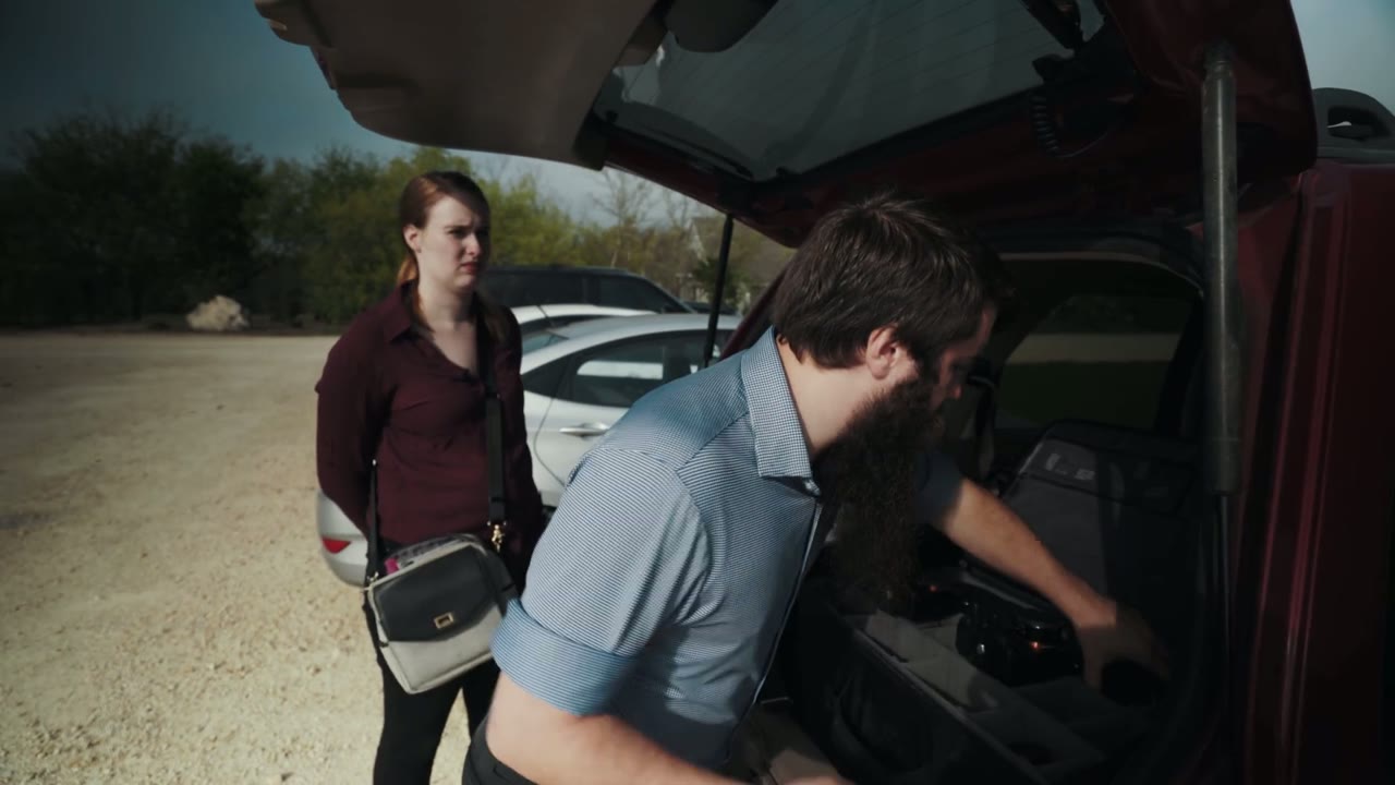 Matt pulling gear from the open trunk while Rachel stands beside him holding a shoulder bag