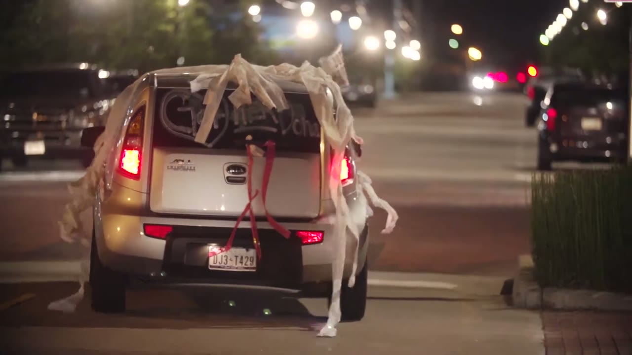 Getaway car driving off at night with white streamers and a red bow tied to the rear bumper