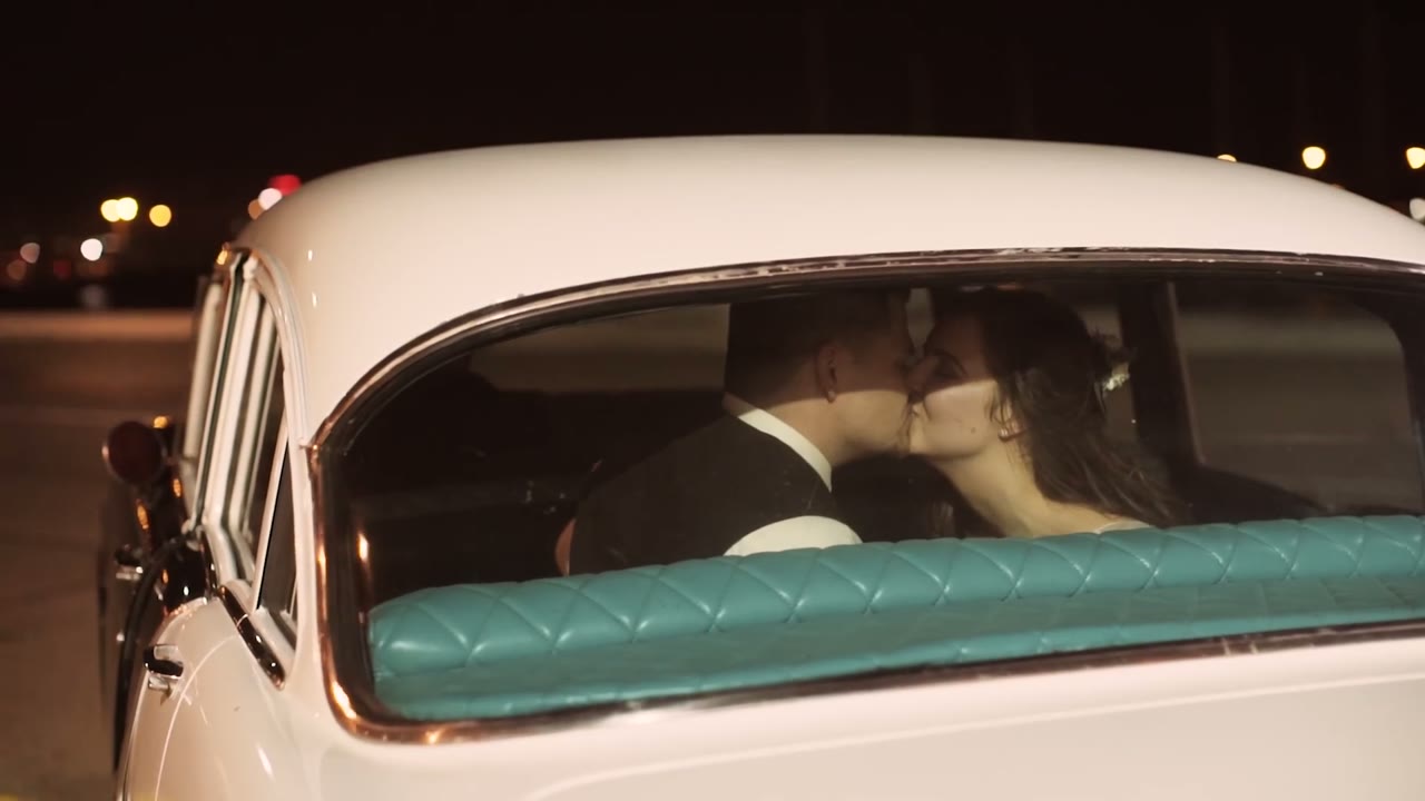 Bride and groom kissing in the back seat of a vintage white getaway car with teal upholstery at night