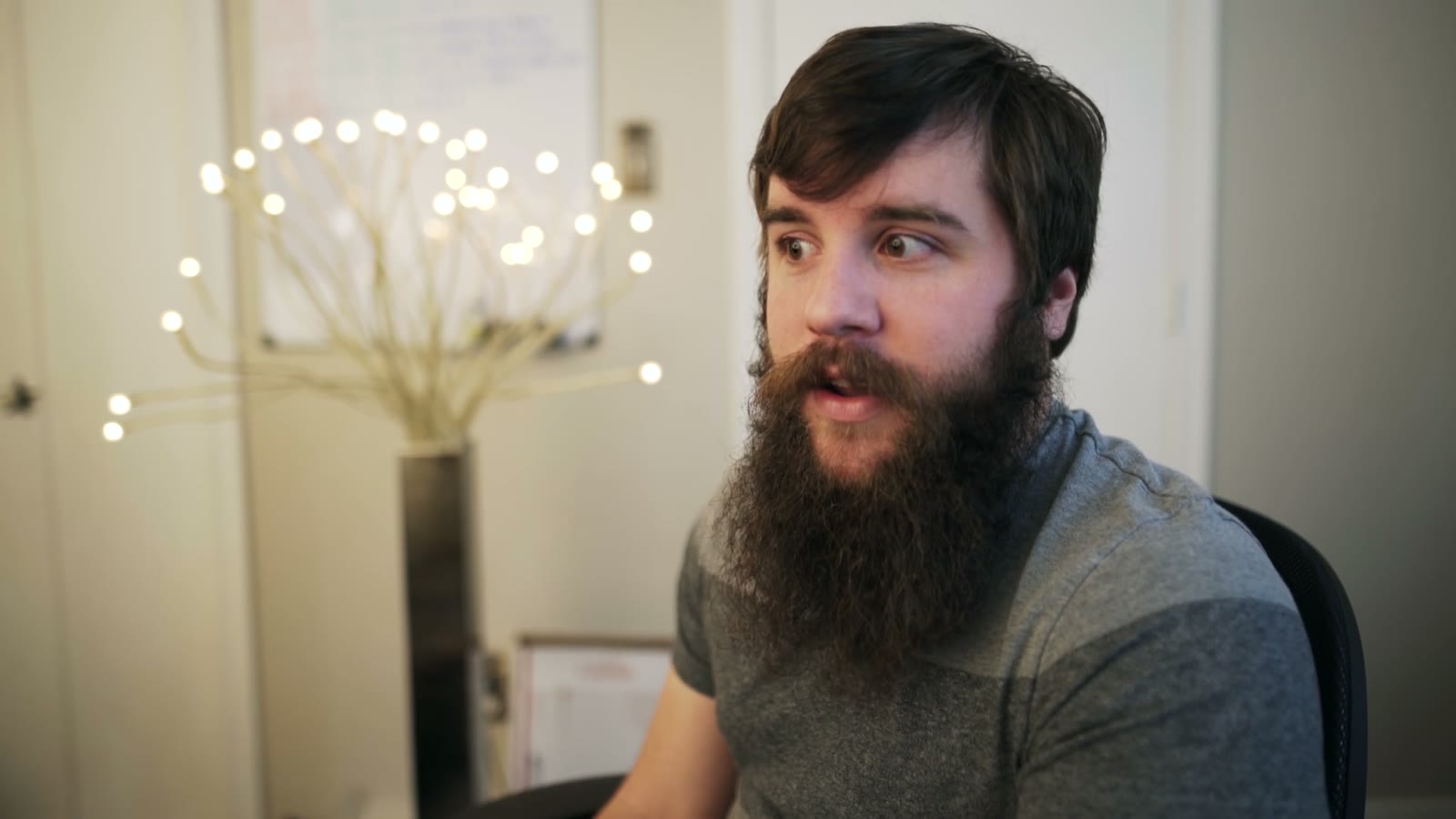 Bearded man in profile with mouth open and eyebrows raised, mid-word looking off to the side
