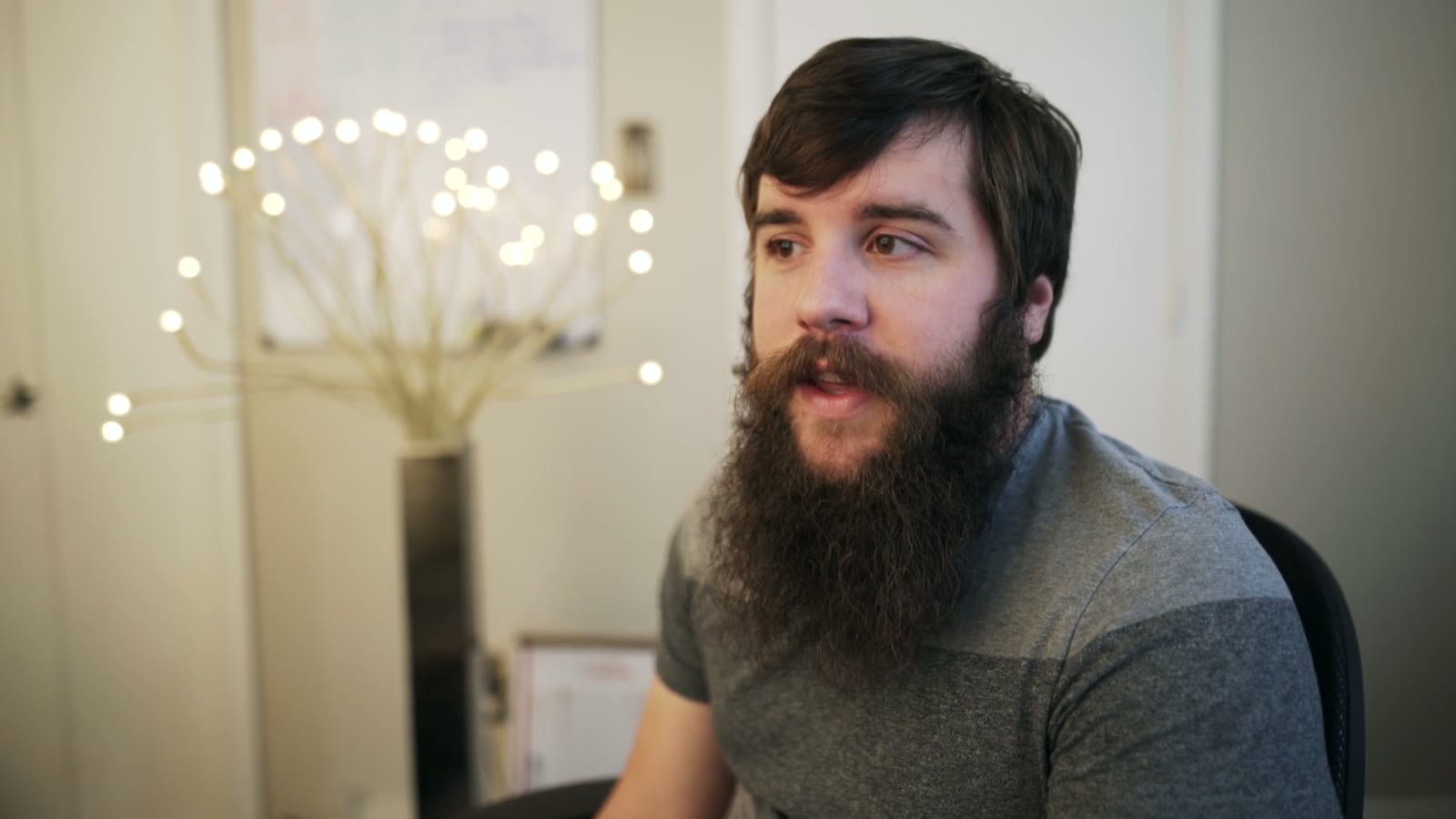Bearded man in profile looking off to the side with a calm, closed-mouth expression while talking