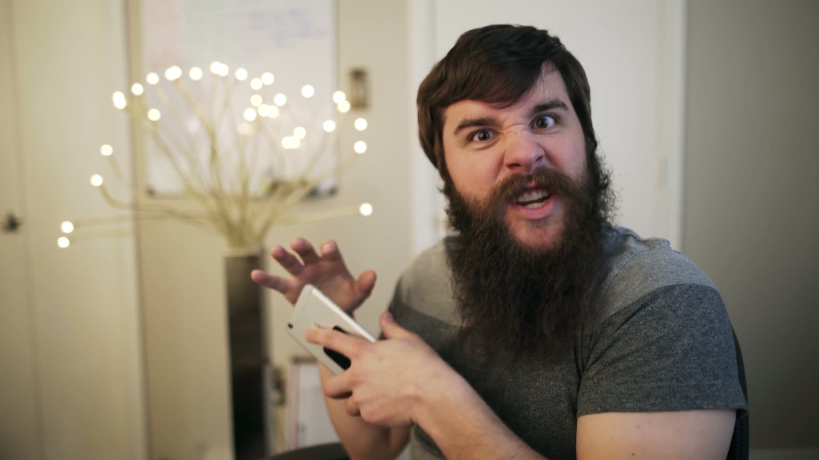 Bearded man reacting with wide eyes and raised eyebrows while holding a white phone in both hands
